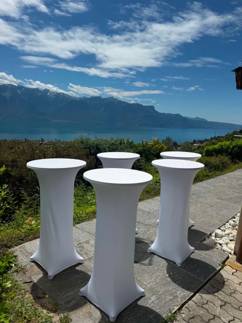 Événement extérieur : tables hautes à housse blanche en extérieur, face au lac et aux montagnes