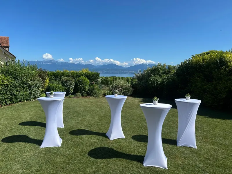 Réception : tables hautes à housse blanche dans un jardin avec vue sur le lac et les Alpes