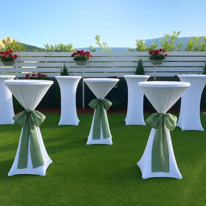 Soirée : tables hautes à housse blanche ornées de nœuds verts sur une pelouse décorée de fleurs