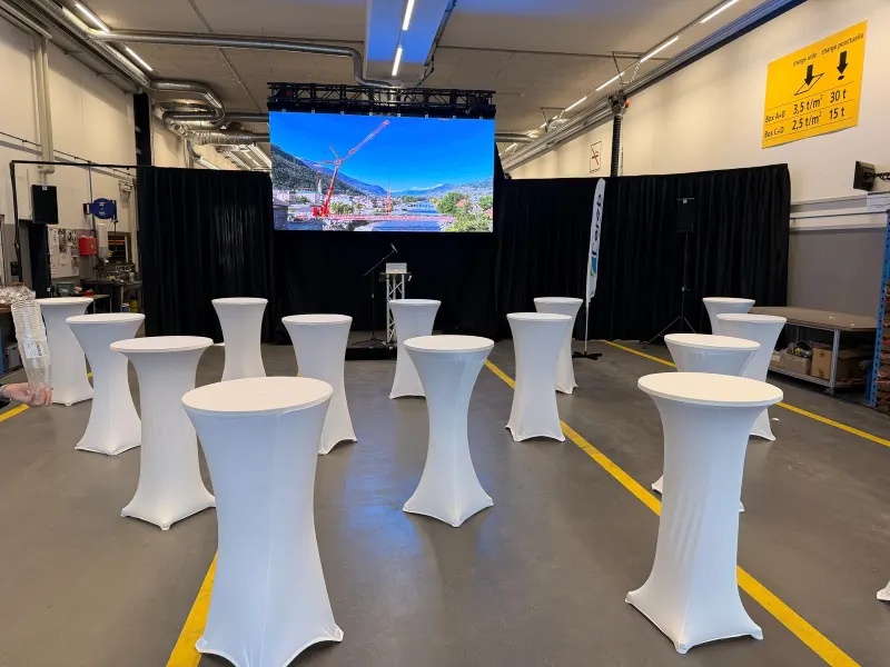 Événement : tables hautes à housse blanche dans un hall d'entreprise avec écran géant