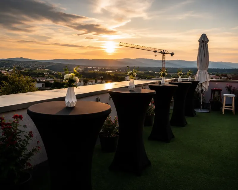 Anniversaire : tables hautes à housse noire décorées de vases fleuris sur une terrasse au coucher du soleil